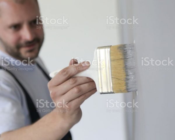 Man painting with a paintbrush over a grey wall